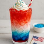 a layered red, white, and blue energy drink served in a clear glass with a straw—perfect for the 4th of July.